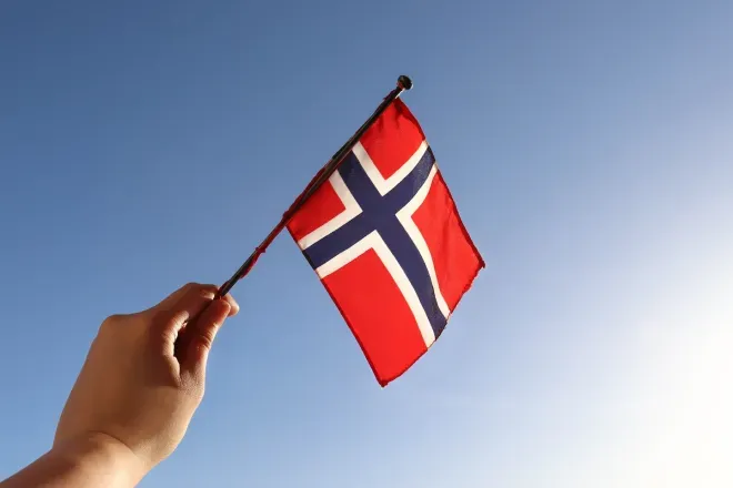 Hand holding Norwegian flag in sky