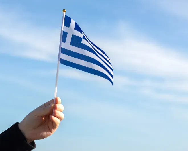 Hand holding Greek flag in sky