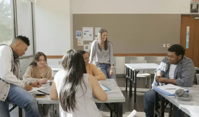 Maestra instruyendo a los estudiantes sentados en pupitres en un aula luminosa.