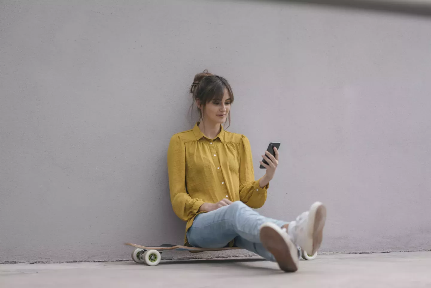 Mujer sentada en longboard mirando su teléfono celular