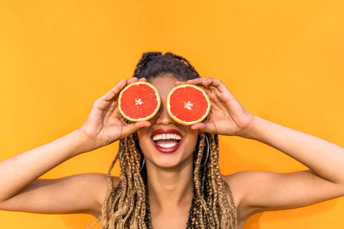 Mujer sosteniendo dos naranjas sobre sus ojos