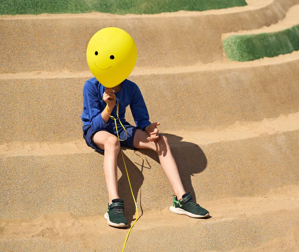 Niño sosteniendo un globo de cara feliz sobre su cara