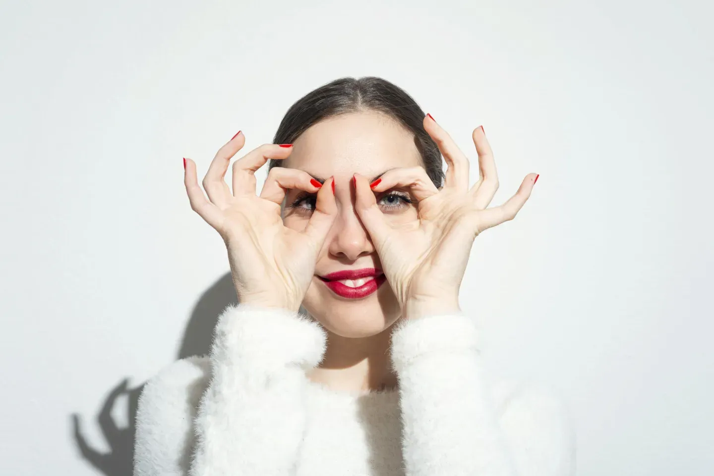 a woman with her fingers in the shape of circles over each of her eyes