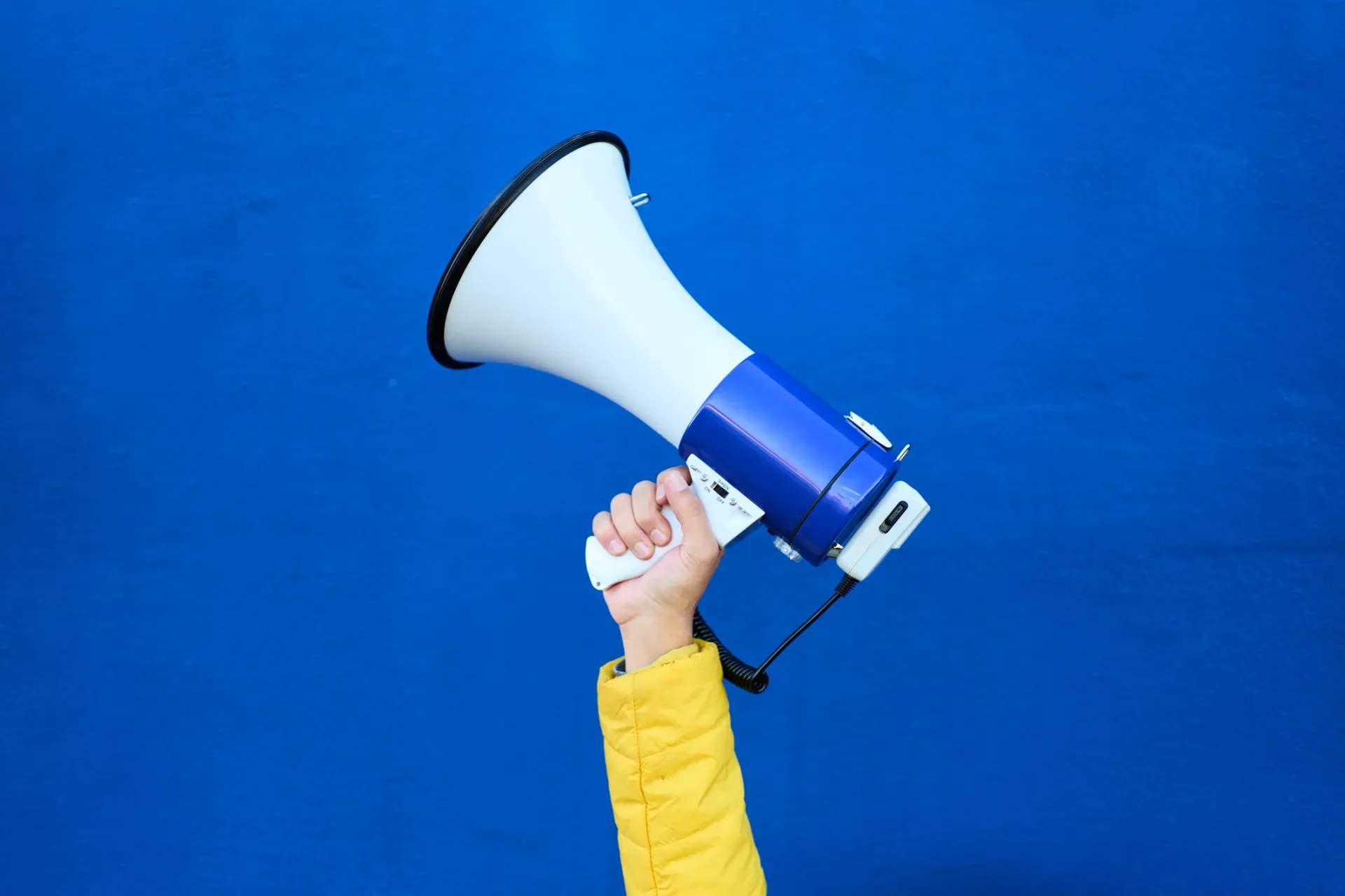 Hand holding white and blue megaphone against bright blue background