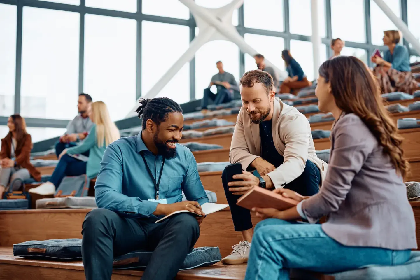 Three diverse college students chatting enthusiastically in a bright, modern lecture hall.