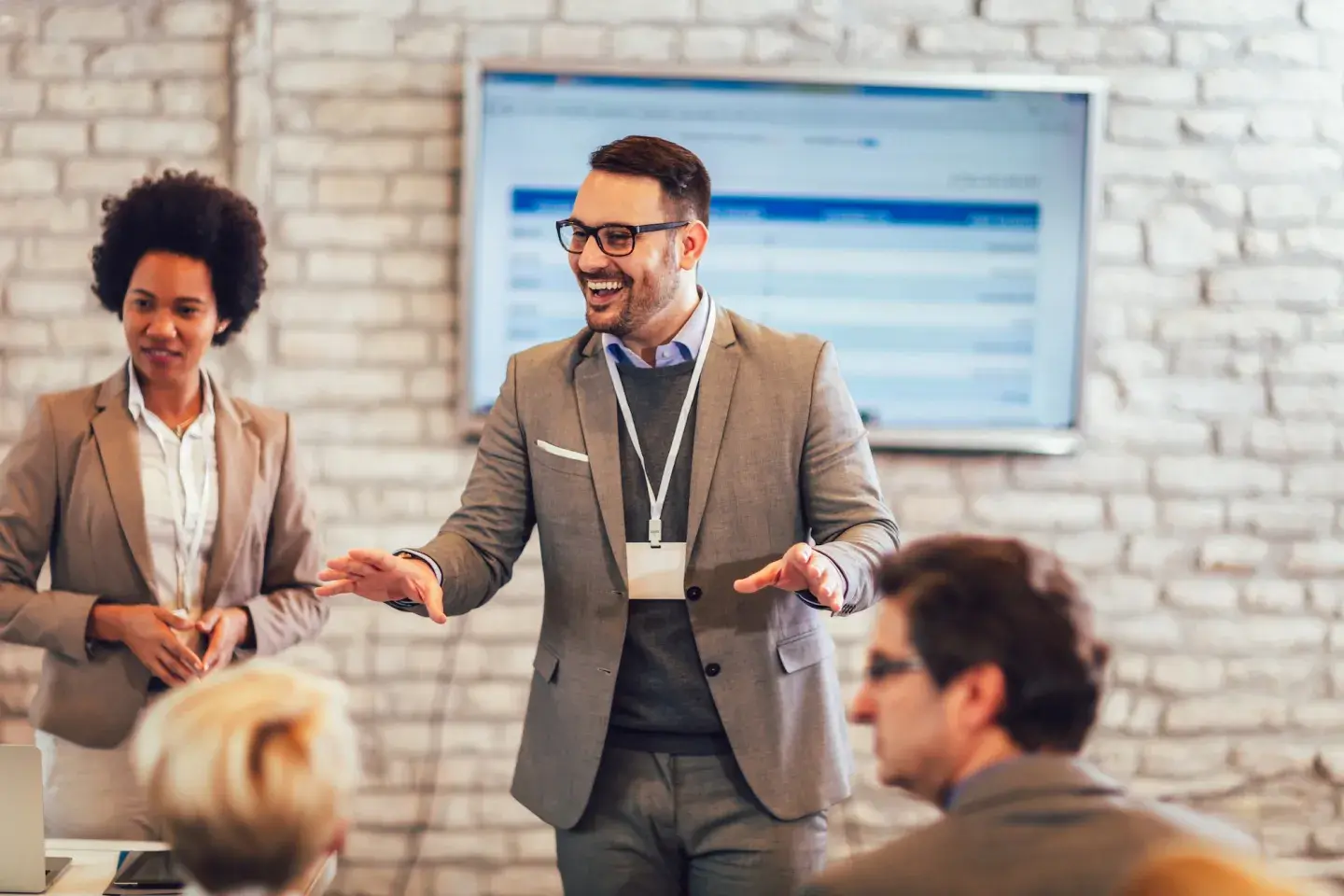 Man in suit with lanyard presenting confidently at a business meeting, colleagues listening attentively. Man in suit with lanyard presenting confidently at a business meeting, colleagues listening attentively.