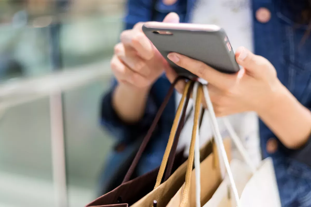 AdobeStock_176193143.jpeg close up of person using cell phone holding shopping bags
