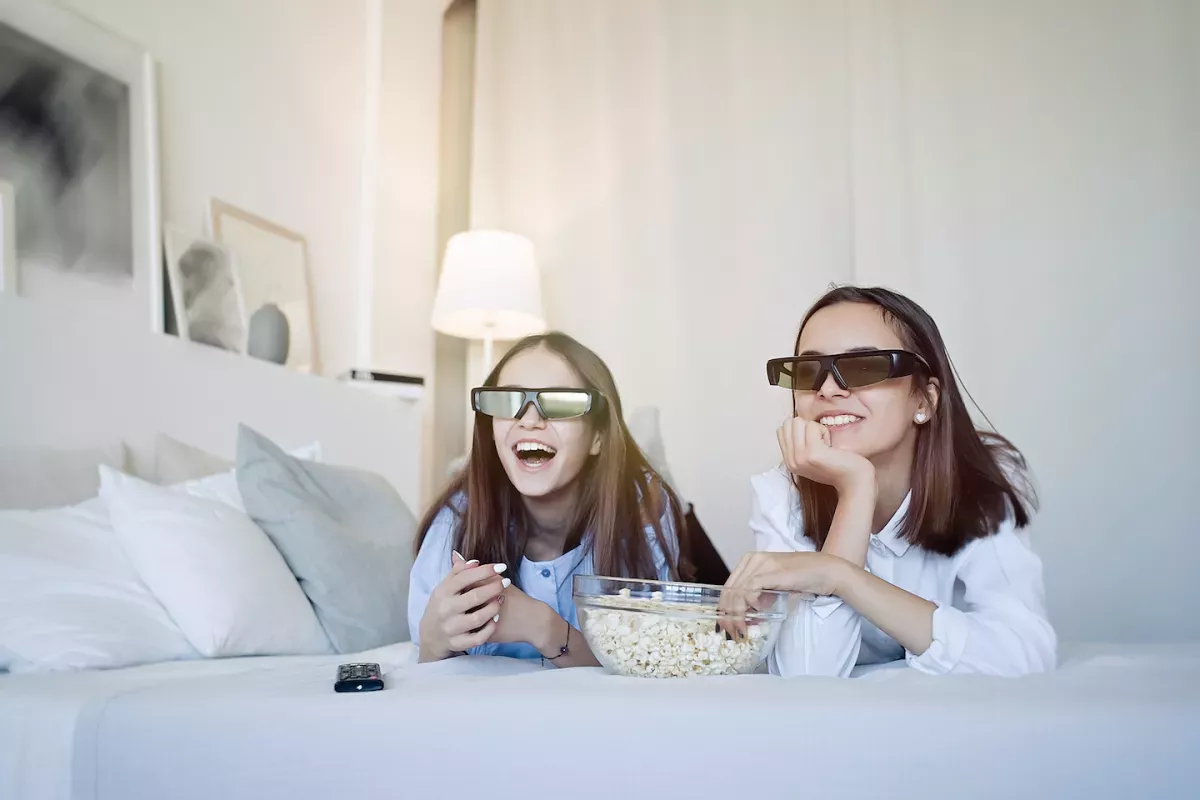 AdobeStock_267580283.jpeg Two girls eating popcorn with glasses on