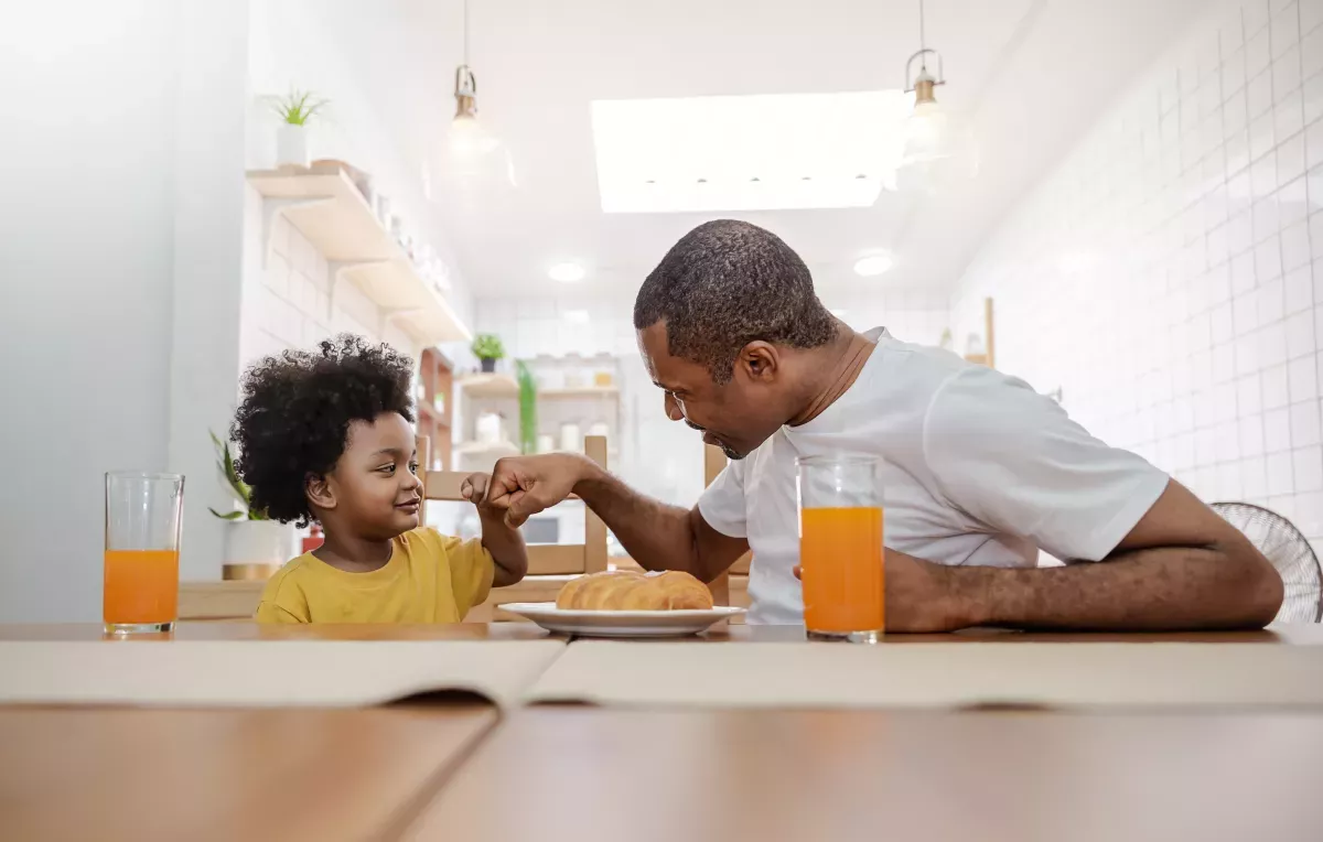 AdobeStock_384069392_Nurture & Manage father and son doing a fist bump during breakfast at kitchen table