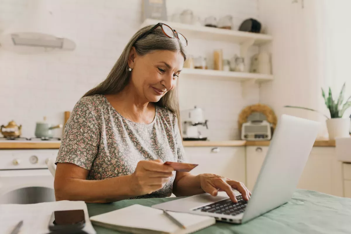 AdobeStock_464117488.jpeg woman using laptop and credit card at kitchen counter