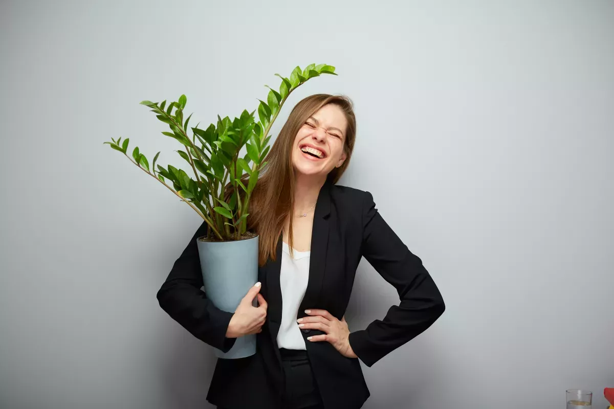 AdobeStock_555543468_Nurture & Manage woman smiling in black suit holding house plant