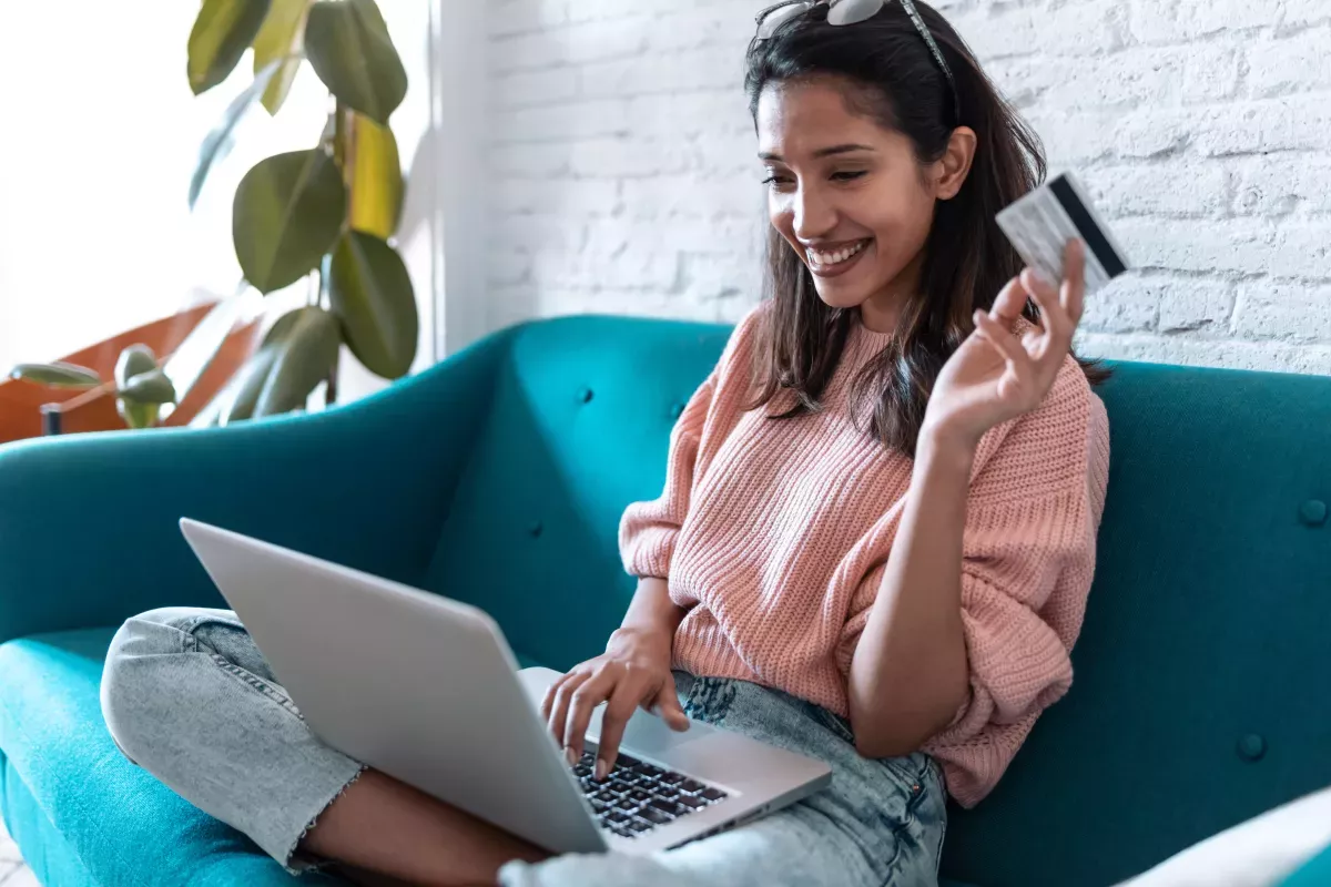 C_16.jpeg smiling young woman on couch with credit card and laptop in hand