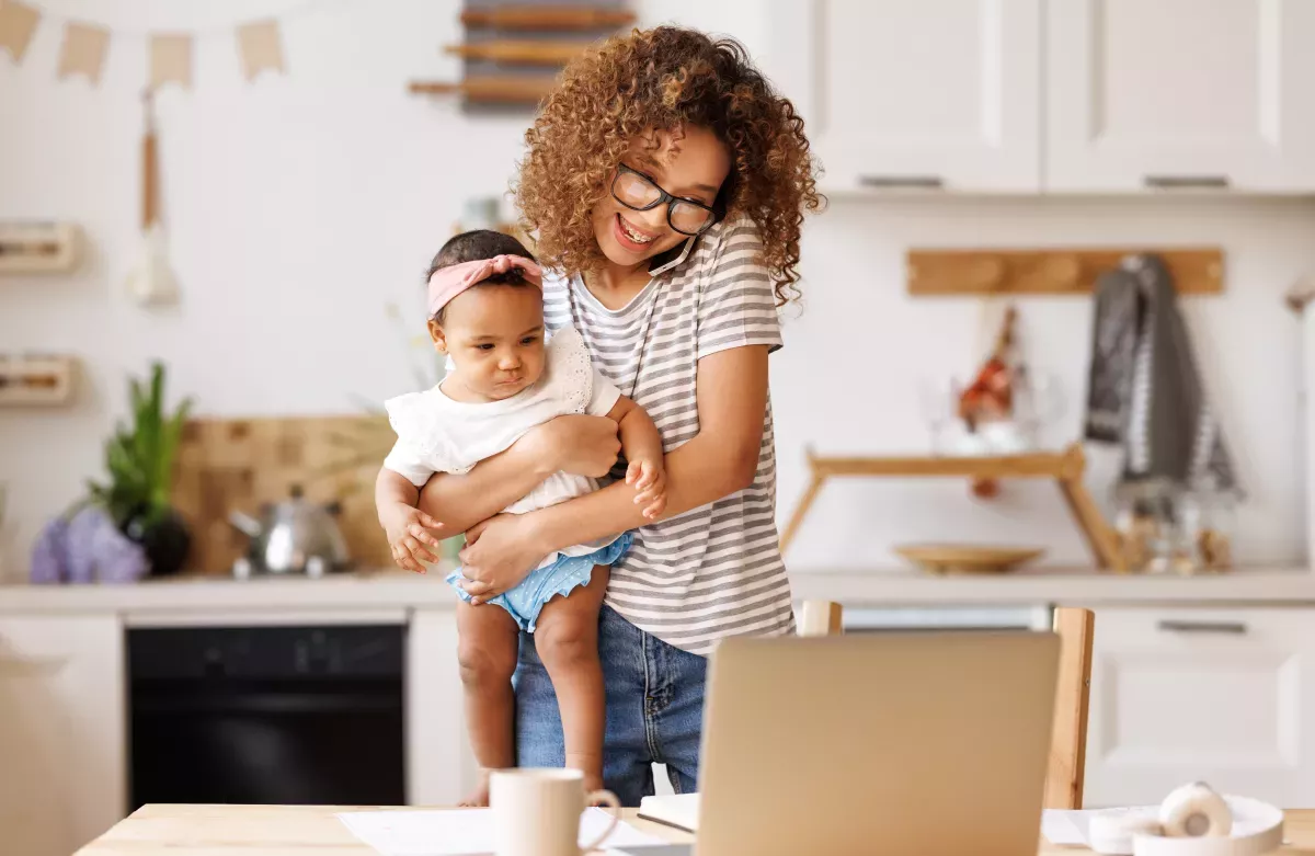 Adobe_494465198_Nurture & Manage smiling mother working from home while holding baby