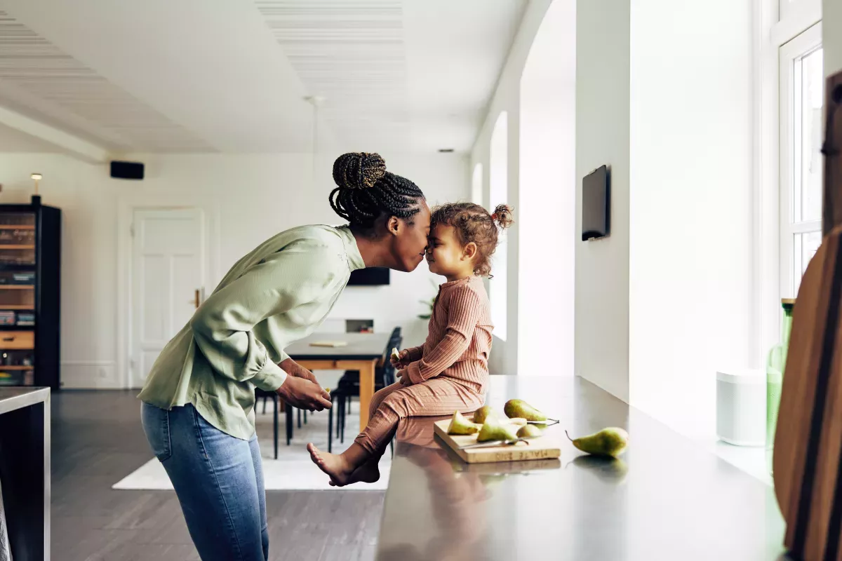 Adobe_415876868_Nurture & Manage mother nuzzling young daughter sitting on the counter enjoying pear snack