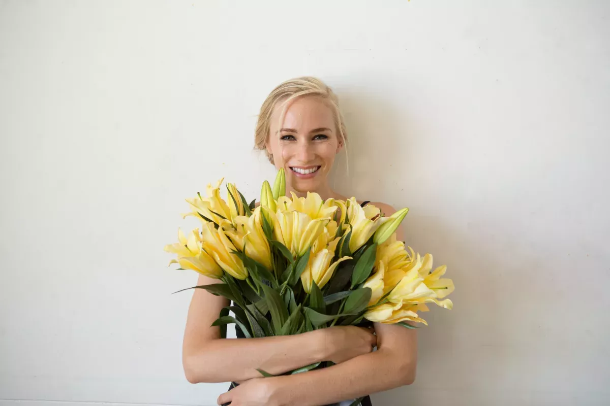 GettyImages-1134420382.jpg smiling young woman hugging a bouquet of yellow lilies