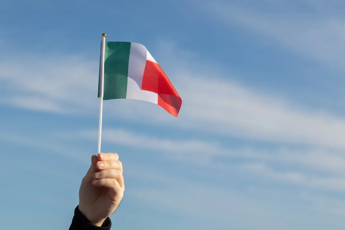 Hand holding Italian flag in sky Hand holding Italian flag in sky