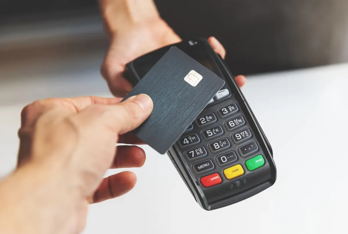 Person's hand inserting credit card into black payment terminal with colorful buttons Person's hand inserting credit card into black payment terminal with colorful buttons