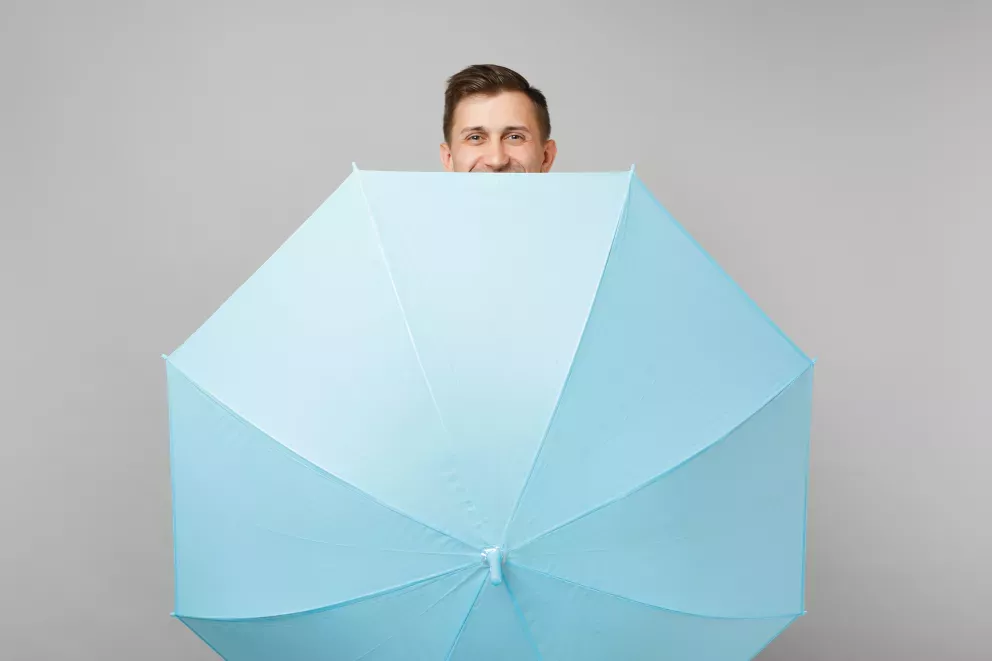 smiling man hiding behind huge blue umbrella 