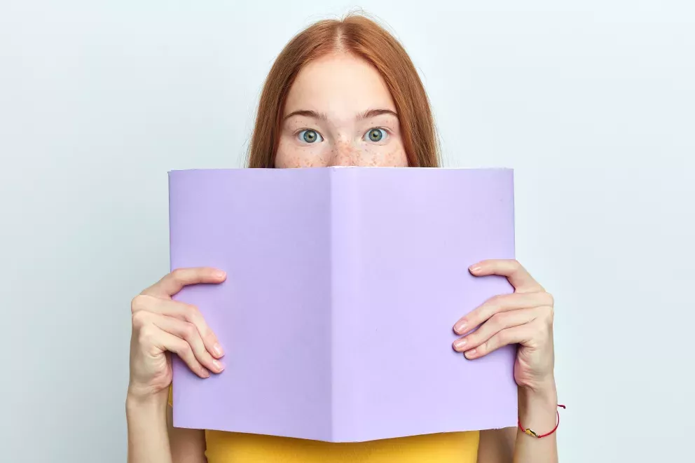 person holding book up to mouth slightly hiding 