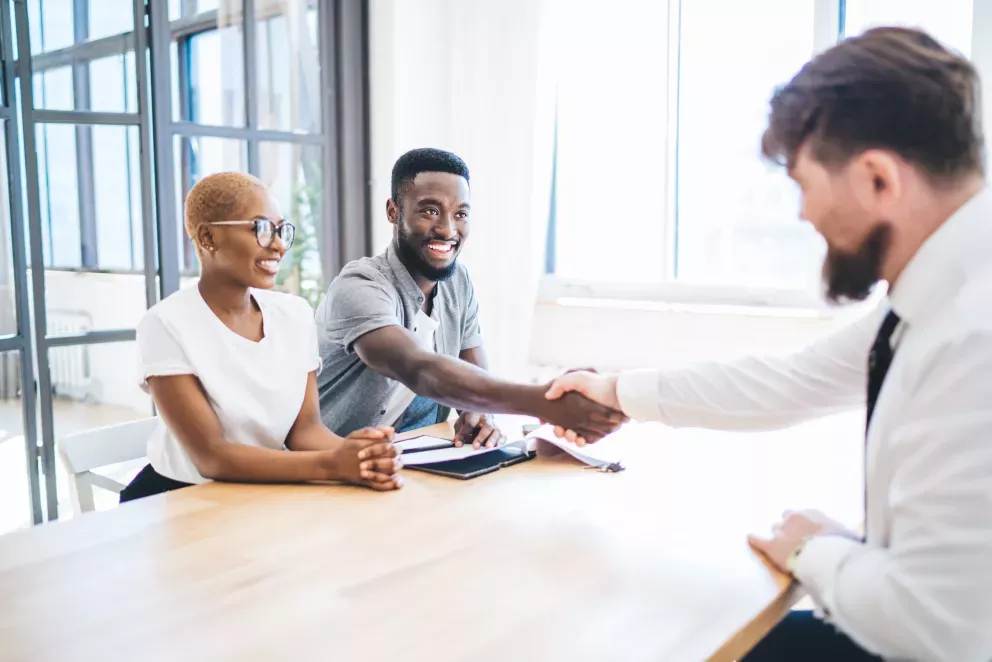 excited young couple shaking hands with business man after signing contract