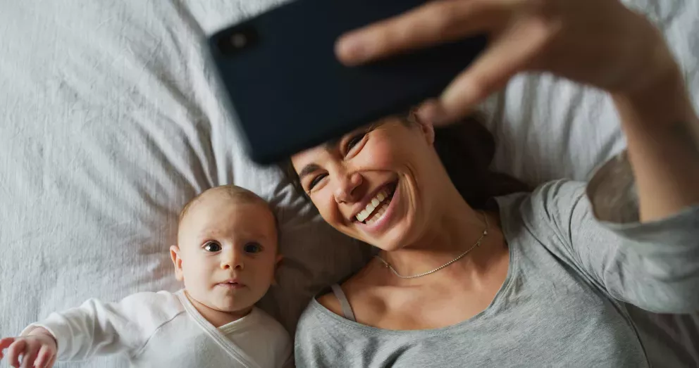 mother and newborn baby taking a selfie in bed