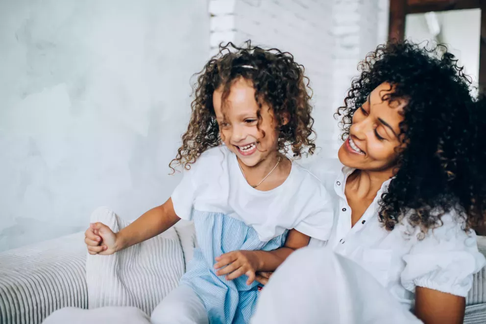smiling mother and child playing on the couch at home