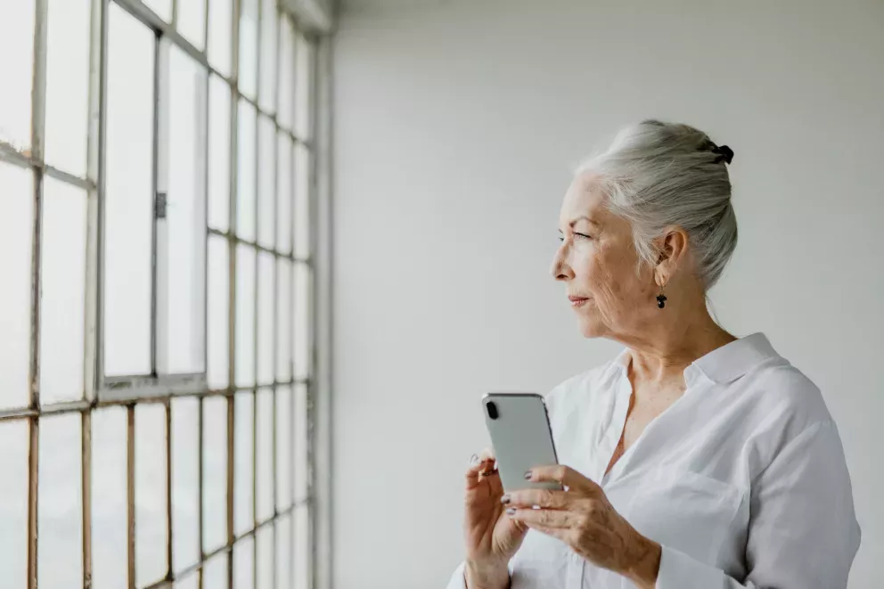 woman looking out window holding cell phone woman looking out window holding cell phone