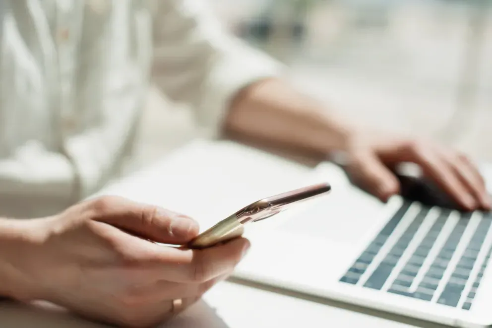 close up of person looking at cell phone while on laptop close up of person looking at cell phone while on laptop