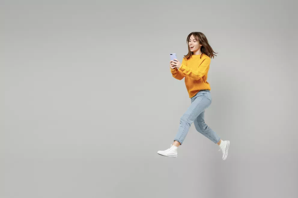 woman smiling leaping with cell phone in hand