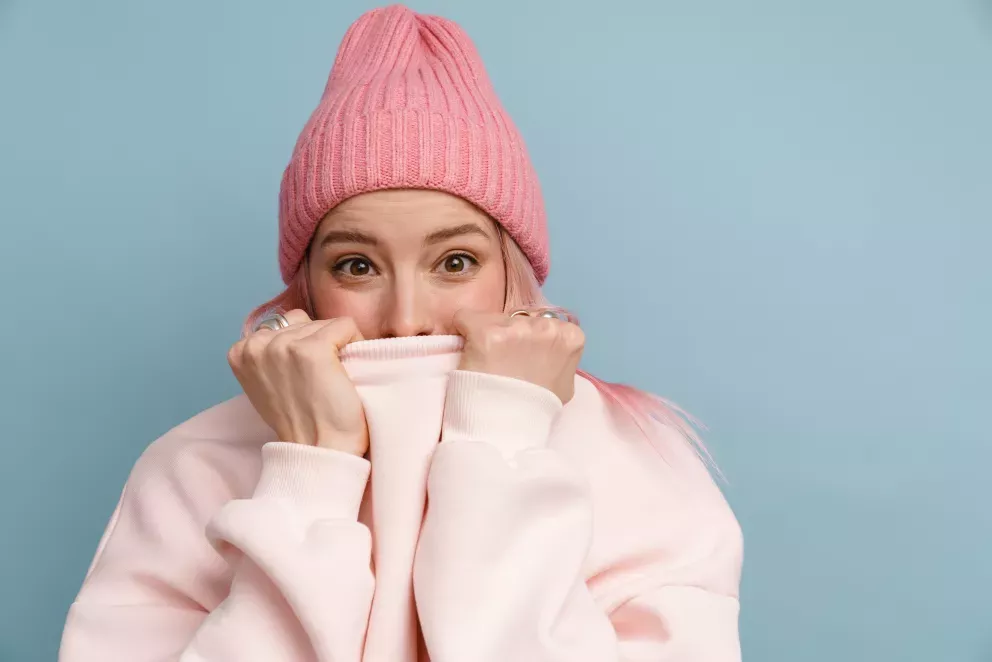 woman with shocked expression hiding mouth by pulling up sweatshirt 