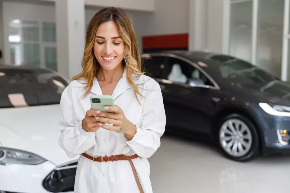 smiling woman customer in car showroom using cell phone