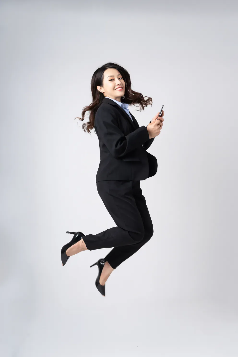 Business woman smiling and jumping while holding cell phone Business woman smiling and jumping while holding cell phone