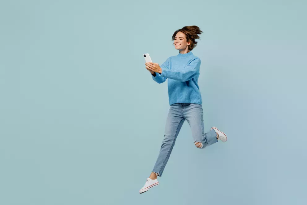 woman leaping through air smiling holding cell phone woman leaping through air smiling holding cell phone