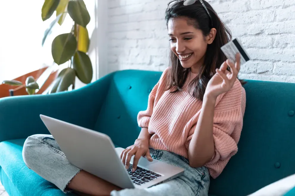 smiling young woman on couch with credit card and laptop in hand