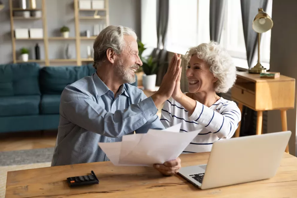 euphoric senior couple giving high five doing domestic paperwork together at home