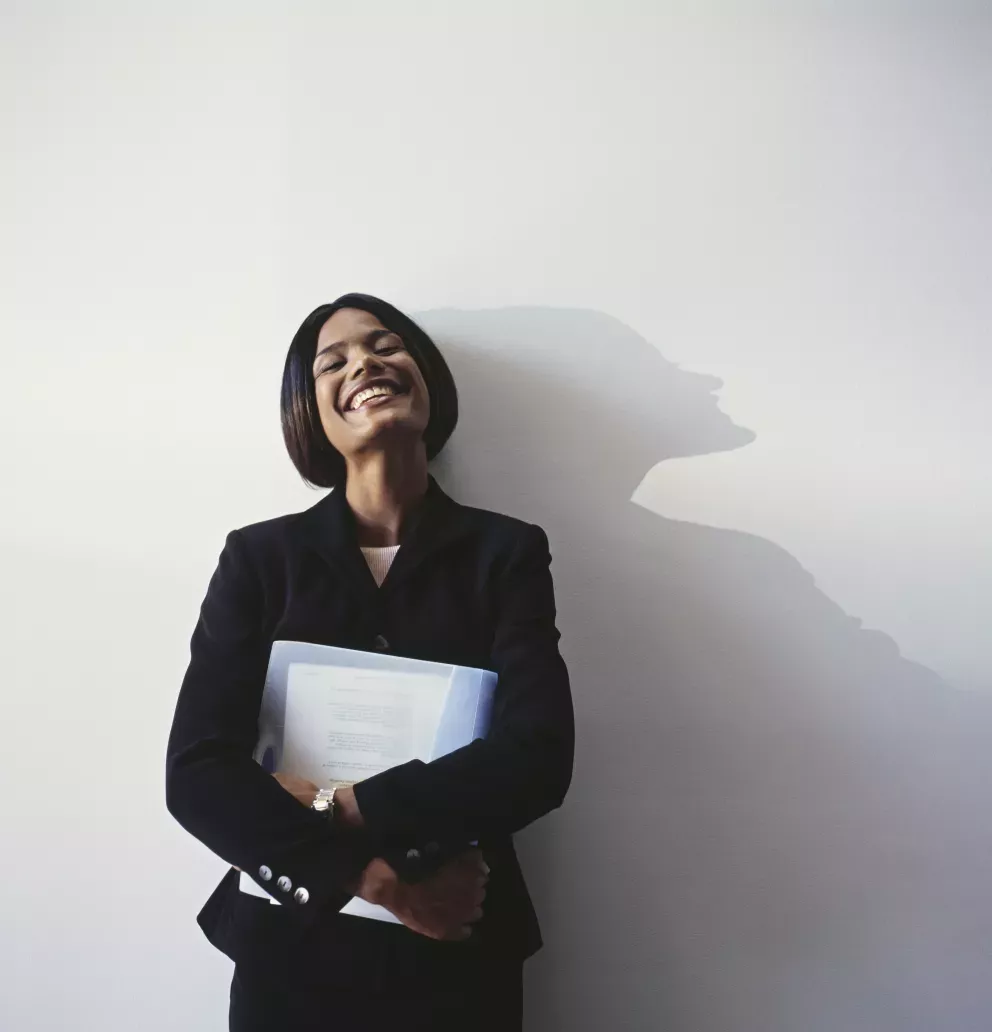 smiling business woman leaning against wall holding binder smiling business woman leaning against wall holding binder