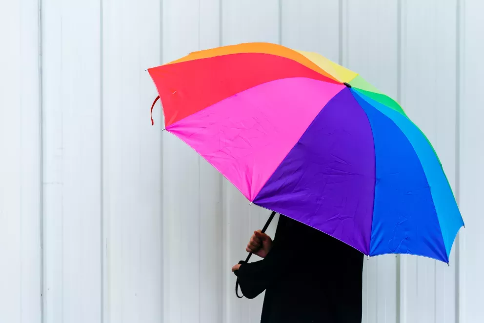 person hiding under big rainbow umbrella 