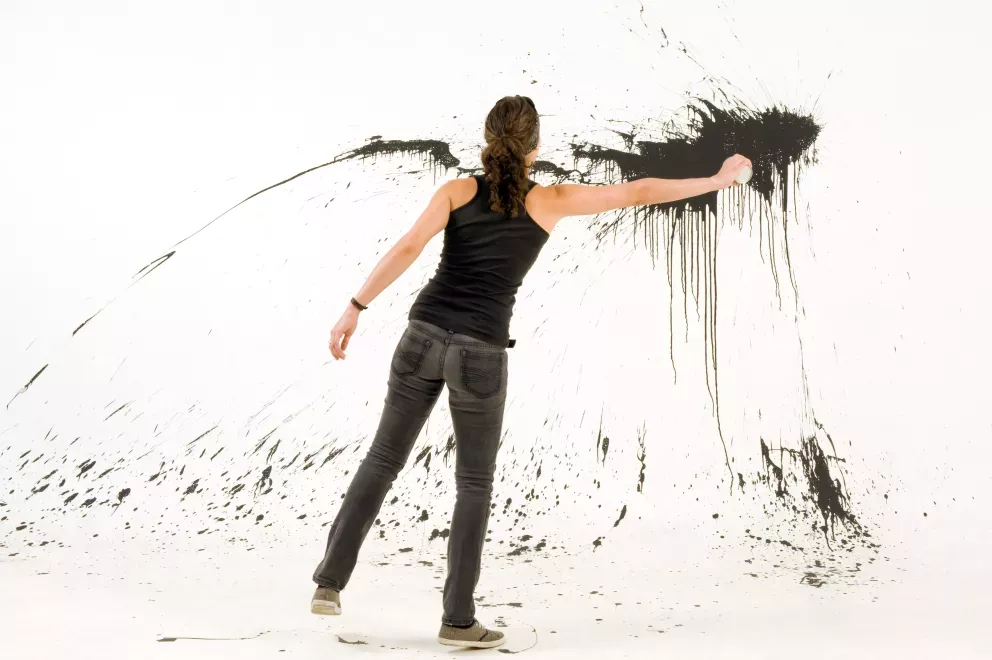artist throwing black paint on white wall