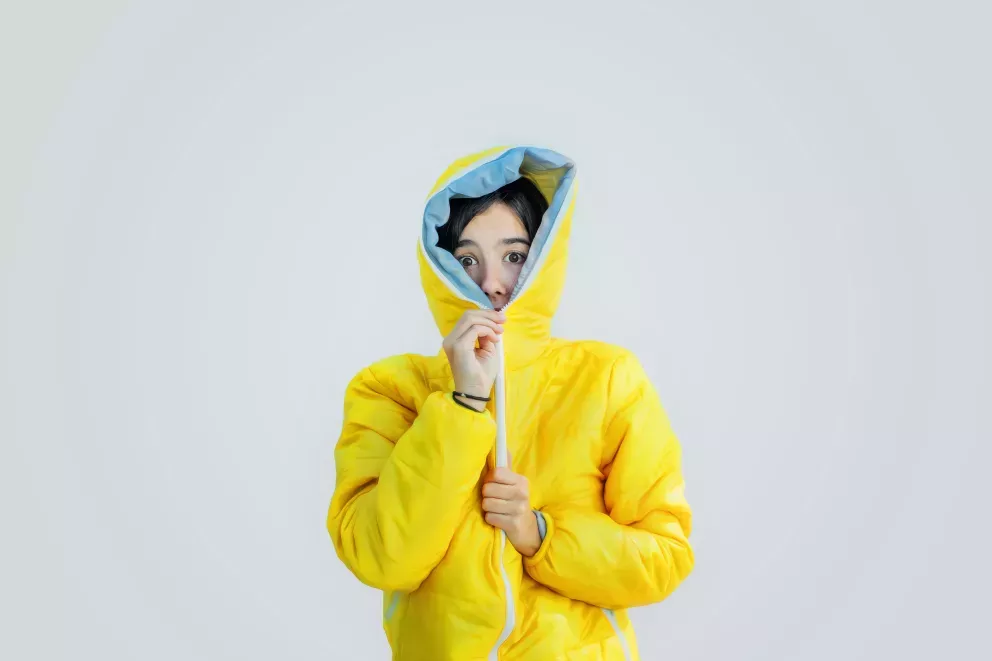 woman zipping bright yellow jacket up all the way covering mouth