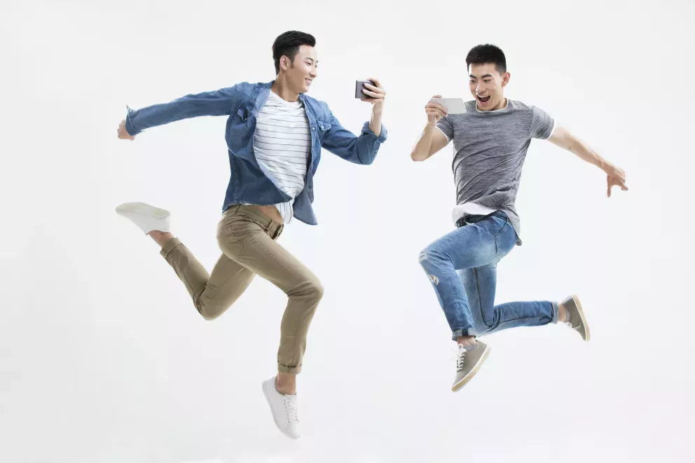 two men leaping and laughing looking at their cell phones