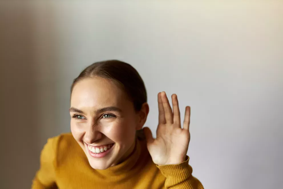 Woman putting hand next to ear listening to funny conversation Woman putting hand next to ear listening to funny conversation