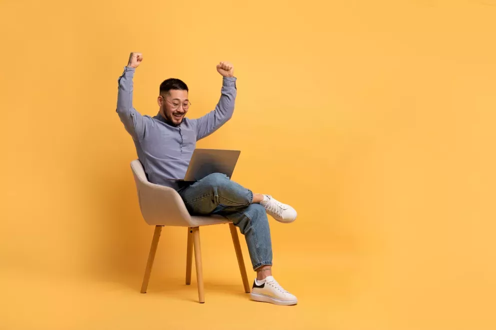excited man sitting in chair with laptop throwing arms up in celebration excited man sitting in chair with laptop throwing arms up in celebration