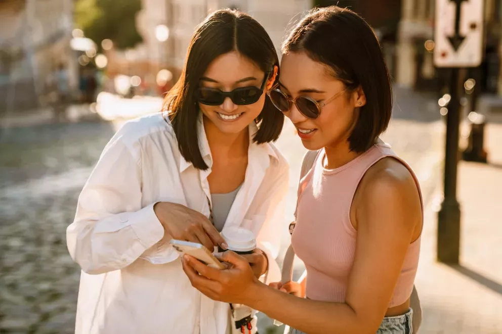 Two women wearing sunglasses smiling and looking at phone together Two women wearing sunglasses smiling and looking at phone together