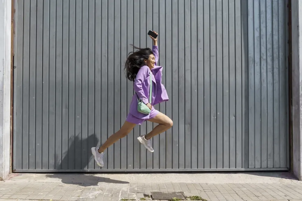 smiling woman leaping holding cell phone
