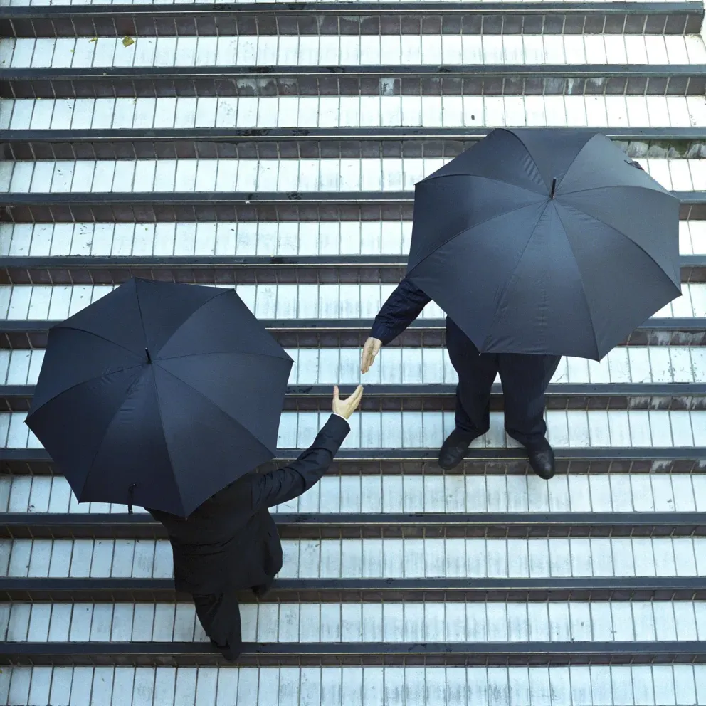 Two men in suits shot from above holding umbrellas and shaking hands