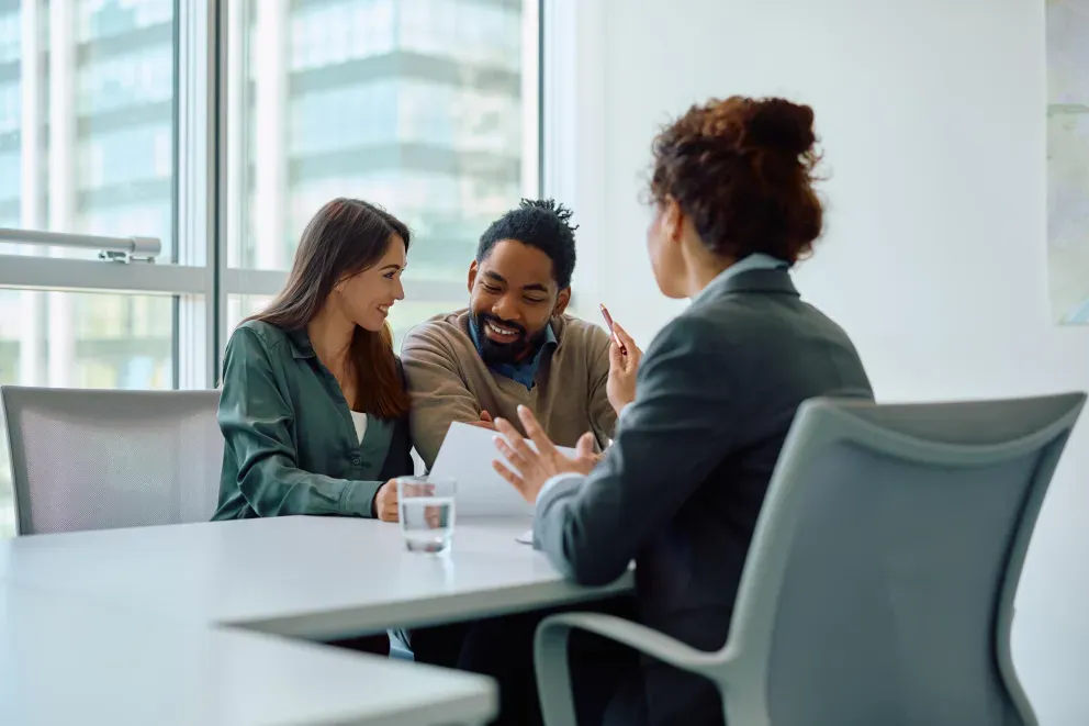 Three people sitting at a desk, reviewing a document, working, and talking