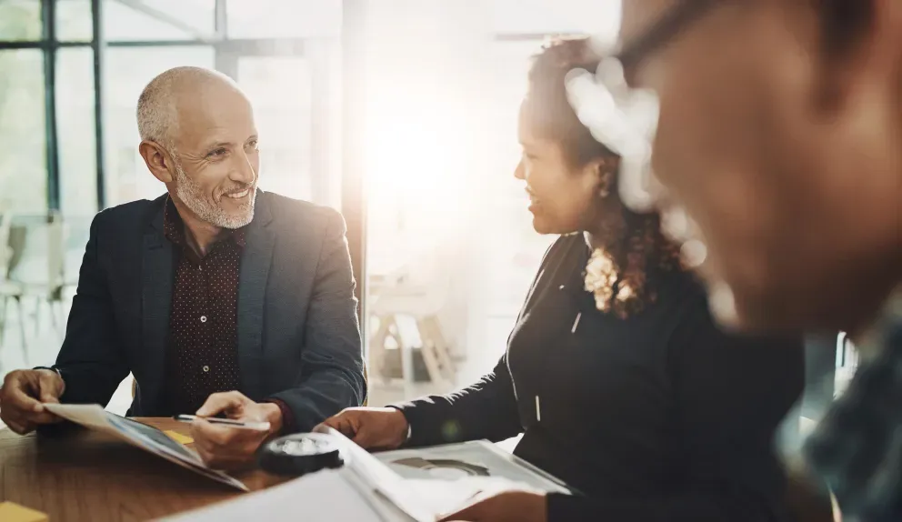 Three people working together at a desk and holding documents