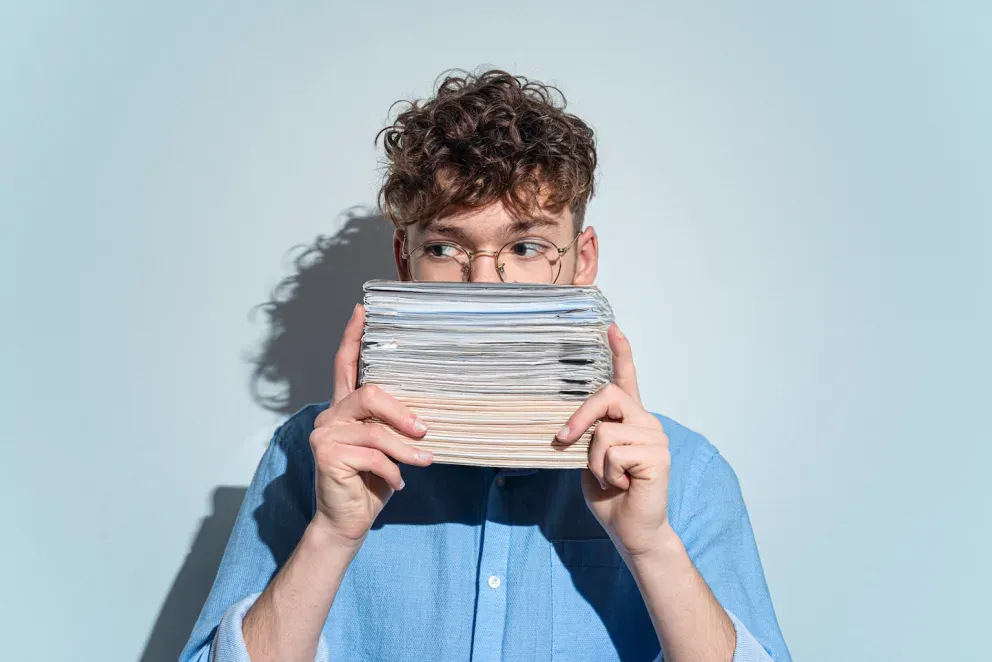 man hiding behind a stack of papers