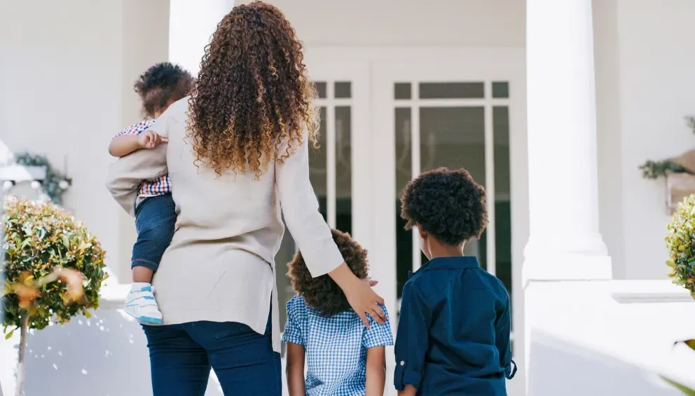 Woman walking with two children towards a white house entrance