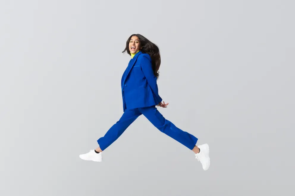 Woman in blue outfit jumping with arms and legs spread against gray background